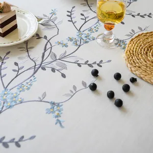 Detail view showing the elegant blue floral embroidery on a premium white linen tablecloth