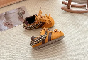 Detailweergave van gele meisjessneakers met geruite ruches en strikaccenten op een tapijt.