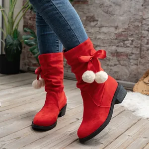 Close-up of red suede mid-calf boots featuring elegant ribbon bows and white pom-poms