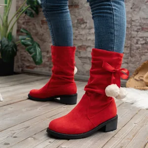 Close-up detail of red suede mid-calf boots featuring a silk ribbon bow and white pom-poms