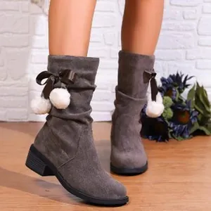 Close-up of grey mid-calf slouch boots featuring white pom-poms and bow details.