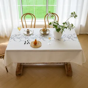Elegant floral embroidered beige tablecloth with decorative tassel fringe on a dining table.