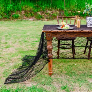 Détail d'une nappe élégante en dentelle française noire sur une table de jardin en bois.