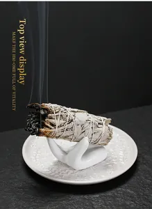 Close-up van brandende witte salie smudge stick op een witte keramische handhouder.