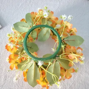 Macro detail of orange wildflower candle ring with green leaves on linen background.