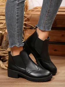 Nahaufnahme von schwarzen Chelsea-Boots mit Brogue-Details und Blockabsatz am Model.