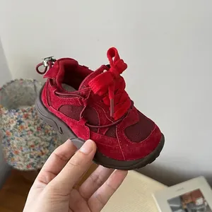 Detail view of a red mesh child's sports sneaker with suede overlays and thick brown sole