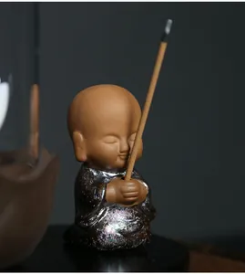 Close-up of a serene ceramic little monk figurine incense burner holding a lit incense stick
