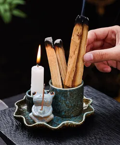 Close-up of ceramic frog incense burner set with burning Palo Santo on dark table