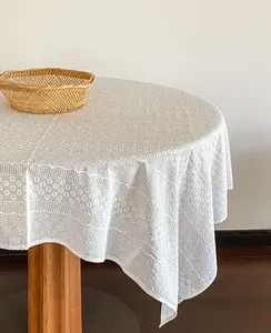 Detailed view of white French embroidered lace tablecloth on a round wooden table