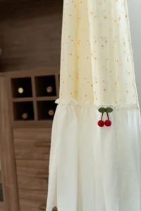 Close-up of fabric curtain with yellow daisy print and red cherry pendant detail