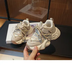 Close-up of stylish children's cream chunky sneakers held by hand in a studio setting.