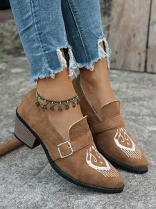 Gros plan de mocassins pointus en daim marron avec broderie blanche et boucle argentée