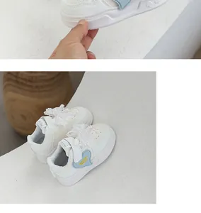 Close-up detail of white girls' sneakers featuring blue heart and pearl bow accents.