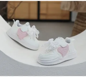 Detailed macro view of girls' white sneakers featuring pearl bow and pink heart decoration