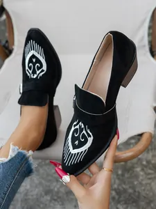 Gros plan de mocassins noirs à bouts pointus avec broderies blanches et talon épais.