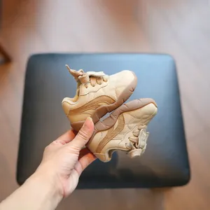 Paar beige en bruine baby-loopschoenen met zachte zool die in de hand worden gehouden