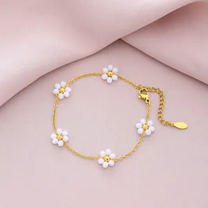 Detailed view of a gold titanium steel bracelet featuring six-petal white flower charms.