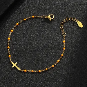 Detailansicht eines goldfarbenen Edelstahl-Kreuzarmbandes mit orangen Emaille-Perlen