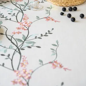 Close-up detail of delicate pink floral embroidery on a premium white linen tablecloth