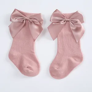 Detailed view of baby knee-high socks with large pink satin bows and soft knit texture.