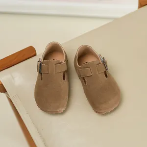 Close-up detail of brown suede kids' clogs featuring an adjustable buckle strap