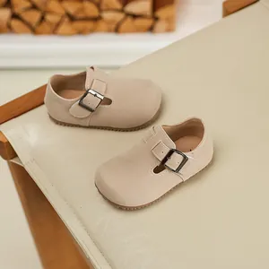Detailed view of beige suede children's buckled loafers resting on a modern cream chair