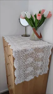 Elegante camino de mesa de encaje bordado blanco sobre una cómoda de madera rústica.