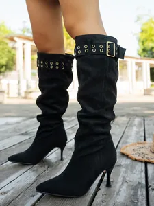Close-up of black suede knee-high boots with stiletto heels and buckle details.