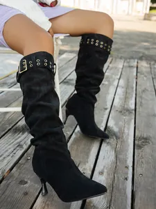 Close-up of black suede slouchy knee-high boots with stiletto heels and buckles