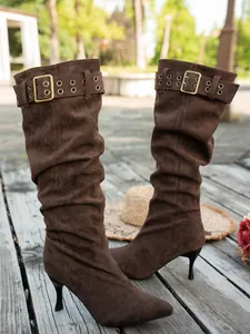 Brown suede slouchy knee-high boots with kitten heels and buckle straps on a wooden deck.
