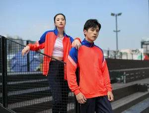 Couple portant des vestes de sport zippées orange et bleu dans un stade extérieur