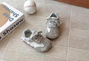 Detailed view of kids' grey T-toe sneakers with lace trim and bow embroidery details.