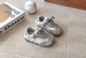 Grey children's sneakers with lace trim and embroidered bow detail on stone tile