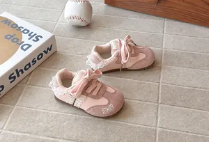 Detail of pink girl's sneakers with lace trim and bow embroidery on tile floor.
