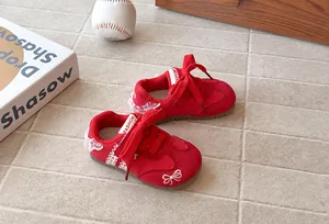 Close-up of red kids retro sneakers featuring lace trim and bow embroidery details