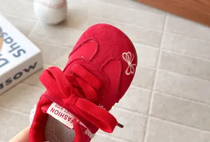 Detail view of red girls sneakers with white butterfly embroidery and lace trim