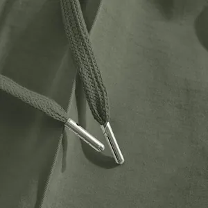 Macro view of olive green drawstring with polished silver aglets on men's casual pants.