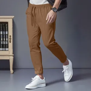 Men's brown slim-fit casual trousers with drawstring waist in a home office setting