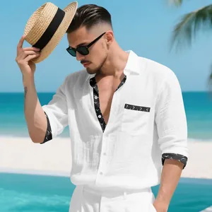 Close-up detail of men's white linen shirt with black patterned trim in a beach setting