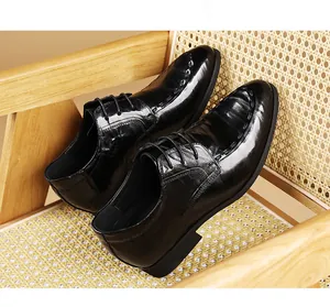 Close-up of black leather business dress shoes with elegant stitching on a rattan chair.