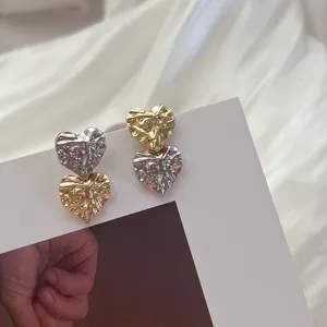 Close-up of heart-shaped earrings with wrinkled texture and two-tone metallic finish