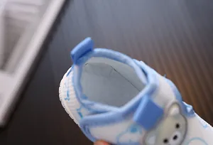 Detalle de zapatos de malla transpirable para bebé con borde azul y oso tierno