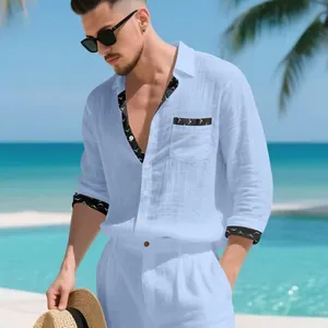 Detail view of light blue linen shirt with black patterned trim in a beach setting.