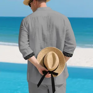 Back view of a grey loose linen shirt for men featuring patterned cuffs on a beach