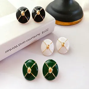 Close-up of vintage enamel stud earrings in black, white, and green with gold trim.