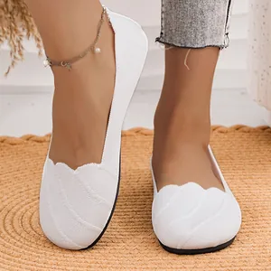 Close-up of white fly-knit flat shoes with scalloped edges and breathable texture