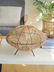 Close-up van handgeweven rotan lampenkap met zwart metalen statief op een tafel.