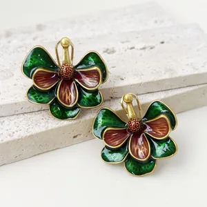Gros plan de boucles d'oreilles fleurs en émail vintage avec pétales verts et rouges.