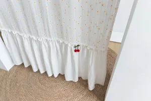 Close-up of red cherry decoration and ruffled hem on a white cotton door curtain.